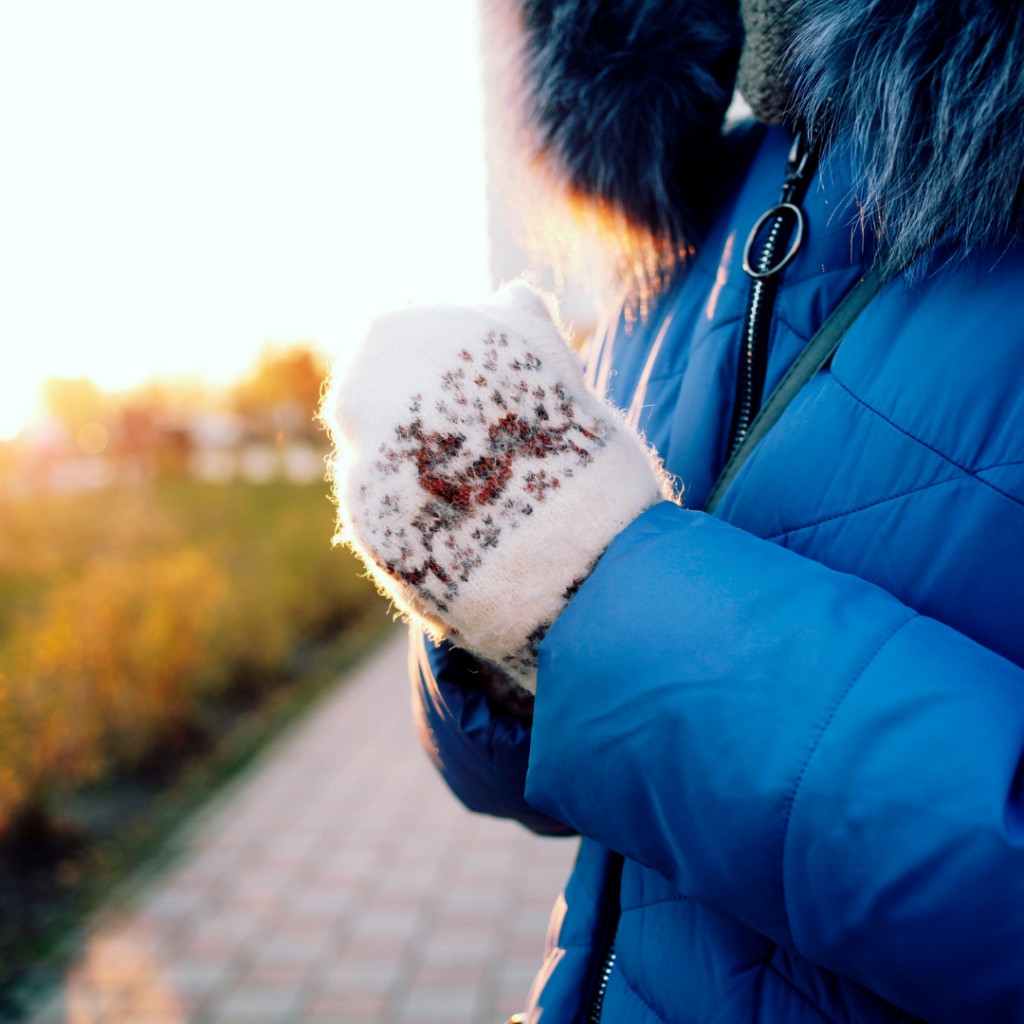 Woman in cold wearing her winter mitts and winter coat trying to stay warm.