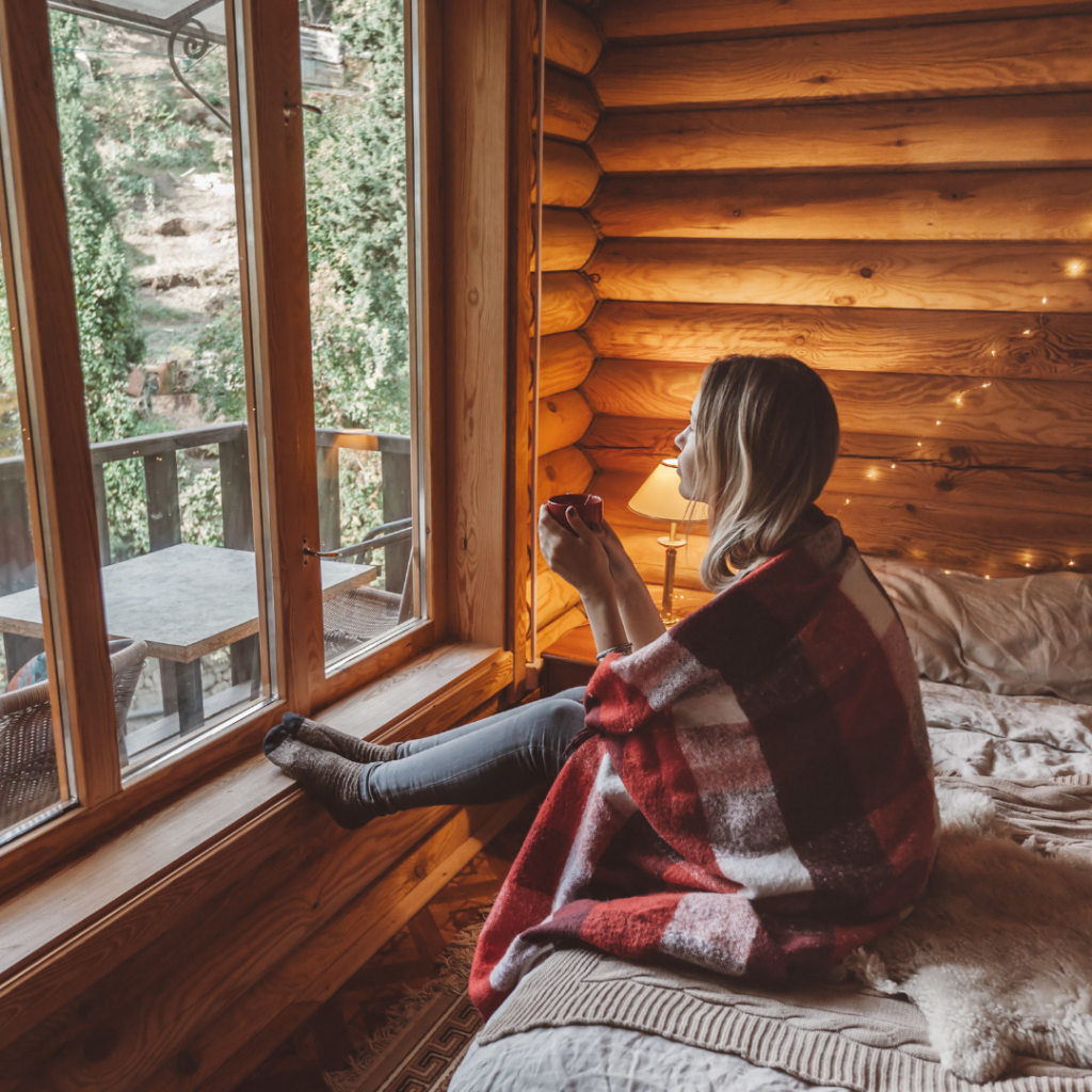 Blonde woman in cabin with blanket and hot coffee trying to stay warm during winter months