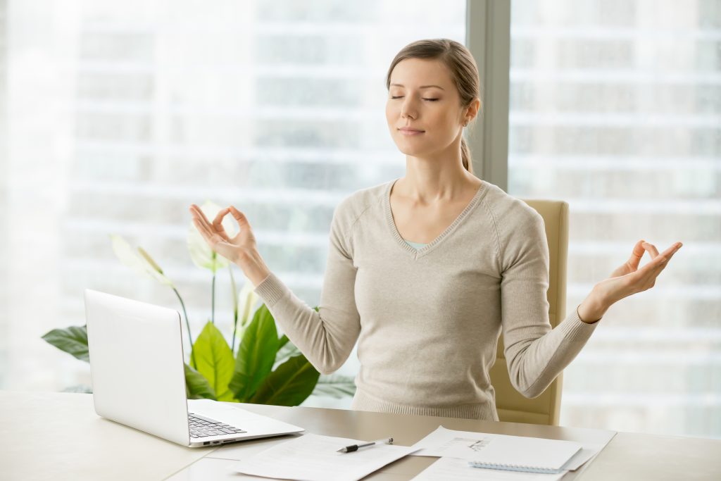 Woman at work desk meditating trying to calm herself down