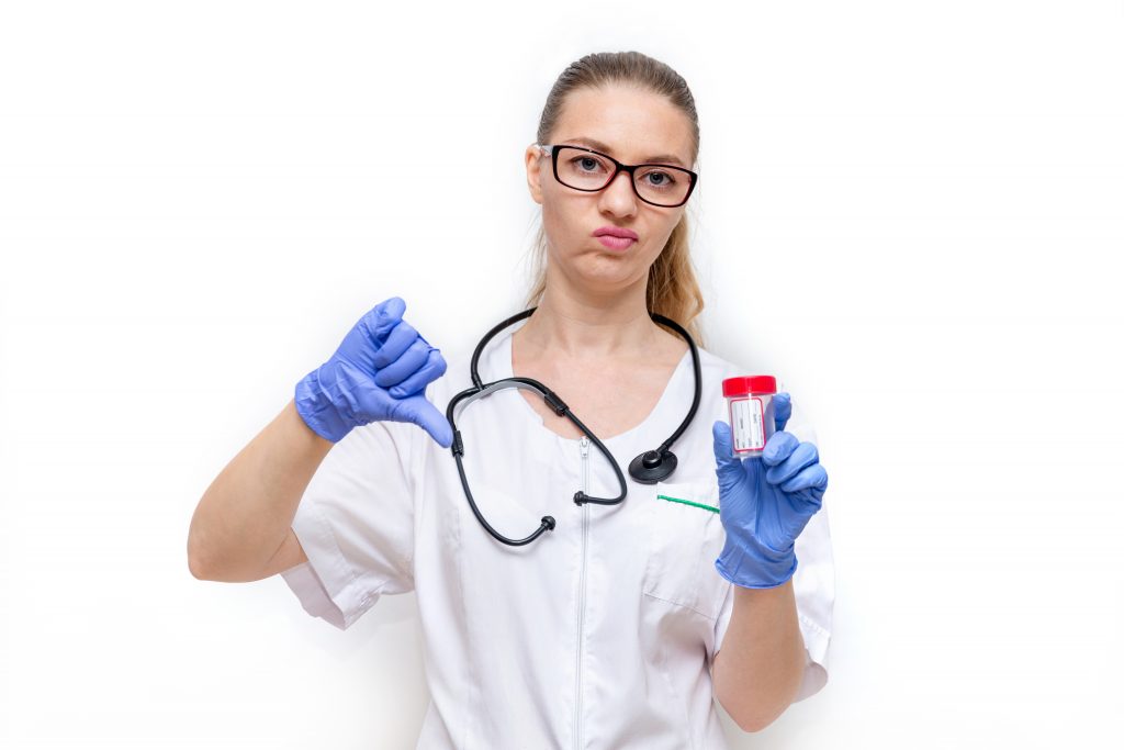 Female doctor in white coat and gloves holds container and shows thumbs down, bad analysis. White background. Timely medical exam and delivery of urine and Feces tests for prevention of diseases