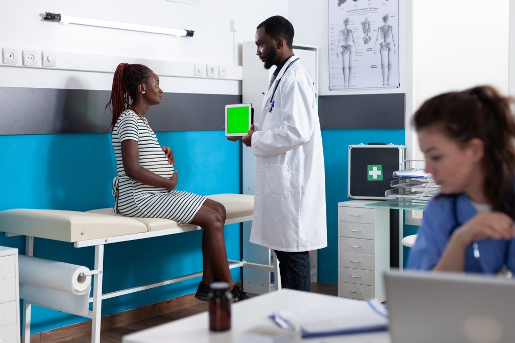 Physician showing tablet with vertical green screen to pregnant woman. adult expecting baby looking at chroma key with isolated template and mockup background for healthcare.