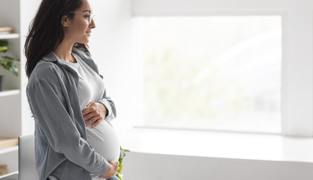 Side view of pregnant woman holding her belly at home with copy space