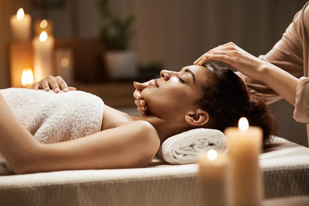 Attractive african girl enjoying face massage in spa salon. Closed eyes.