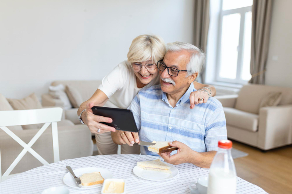 Happy old family couple talking with grandchildren using tablet surprised excited senior woman looking at tablet waving and smiling