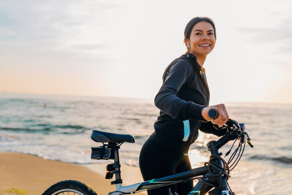 young attractive slim woman riding bicycle, sport in morning sunrise summer beach in sports fitness wear, active healthy lifestyle, smiling happy having fun