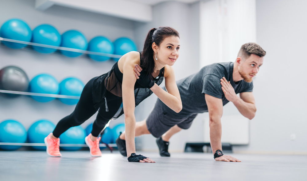 Young couple doing push-ups from floor one hand together