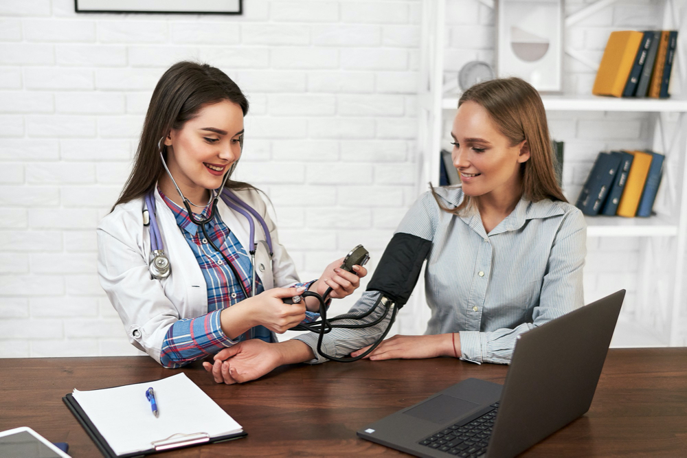 photo beautiful woman at a family doctor measures blood pressure with a tonometer
