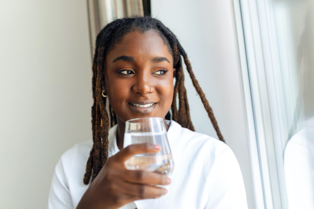 photo young african woman in casualwear drinking water from glass
