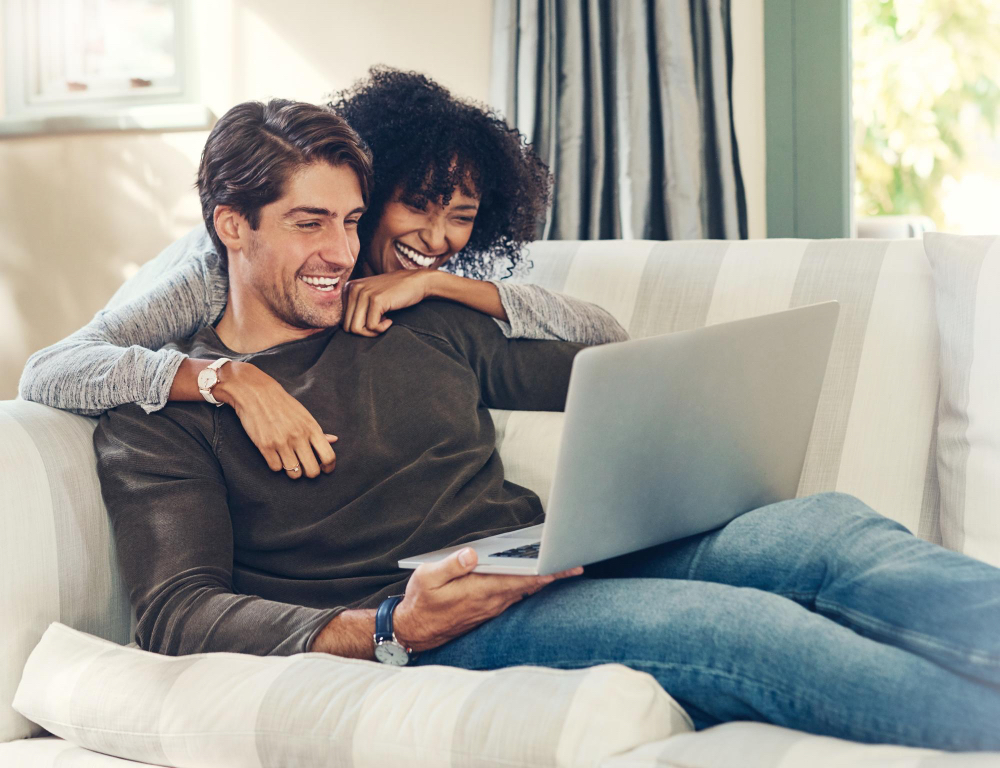 Happy couple relaxing on sofa using laptop together at home.